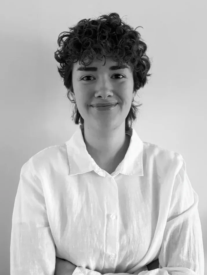 Ei ung kvinne smiler og har på seg hvit skjorte og briller.
